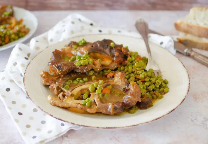 Un saporito ossobuco con piselli e carote, servito su un piatto bianco con tovagliolo a pois.