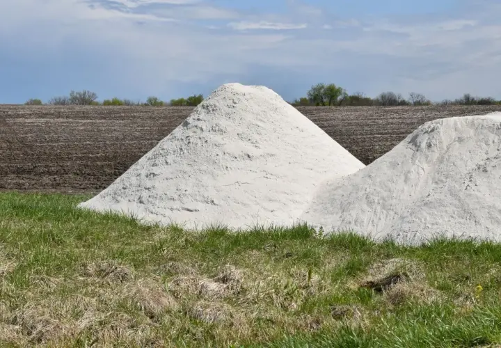 Zwei große Haufen weißes Material, vielleicht Kalkstickstoff, liegen auf einem Feld. Der **Kalkstickstoff Verbot** könnte die Ursache für diese Lagerung sein.