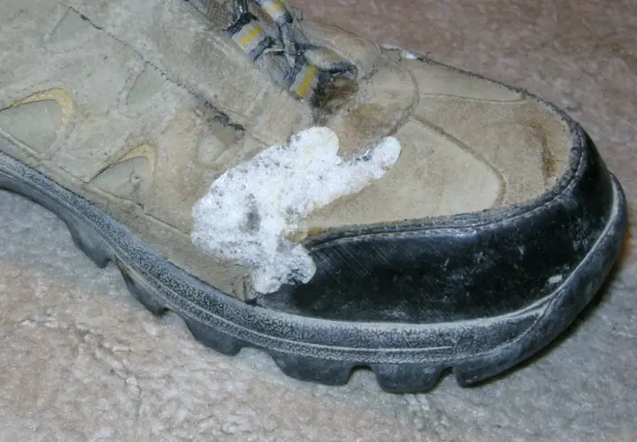 A dirty hiking boot with a white, foamy substance stuck to the side, possibly from a failed attempt to schuhsohle kleben (glue the shoe sole).