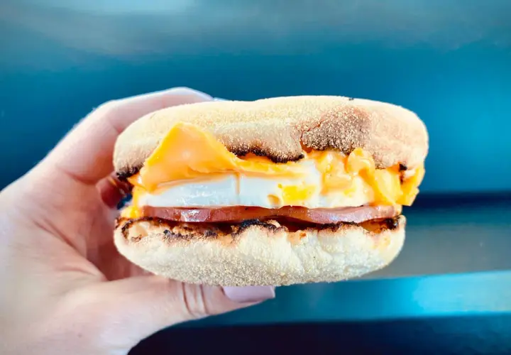 Mcmuffin farmerski z jajkiem sadzonym, plastrem szynki i roztopionym serem, trzymany w dłoni.
