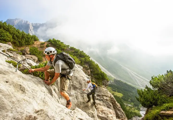 Dwóch turystów pokonuje via ferrata w Austrii, wspinając się po skalnej ścianie z ubezpieczeniem stalowej liny.