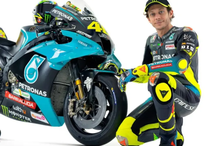 Valentino Rossi posa junto a su moto de competición, luciendo su icónico traje de carreras.