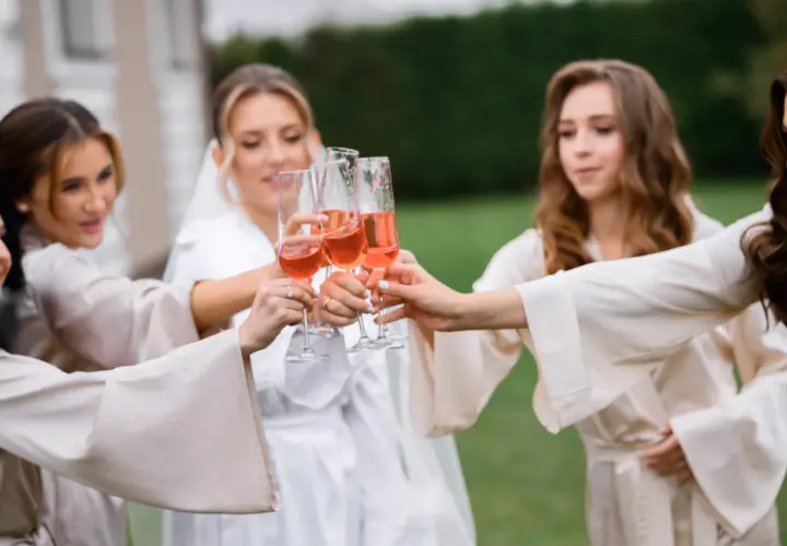 Cinq femmes portent des robes de chambre en soie et portent des verres de champagne rosé pour un vin d'honneur à 16h.