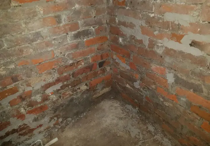 Narożnik piwnicy z ceglanymi ścianami, widoczne ślady prac związanych z hydroizolacją piwnicy od wewnątrz.
