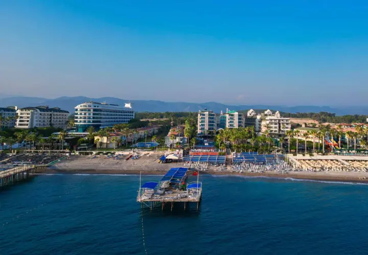 Widok na plażę Concordia Celes Beach z molo, hotelami i palmami w tle.
