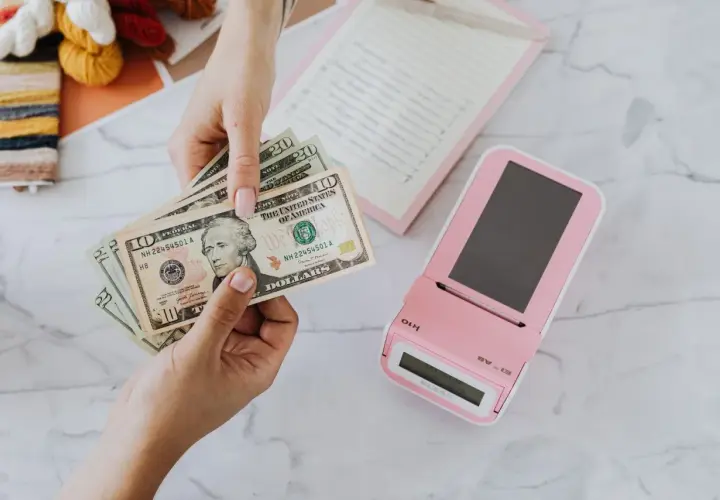 Mani che contano banconote dollari vicino a un registratore di cassa rosa. Un professionista, uno psicologo economico, analizza le spese.