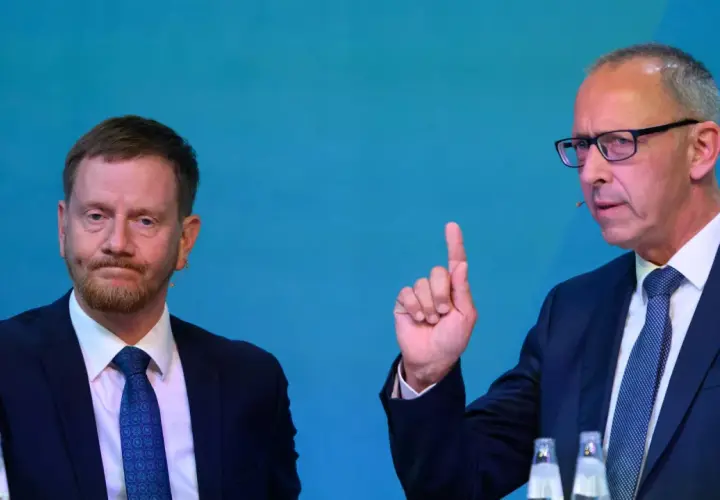 Zwei Männer im Anzug, einer mit Bart, der andere mit Brille und erhobenem Zeigefinger, diskutieren die Wahlprognose Sachsen 2026.