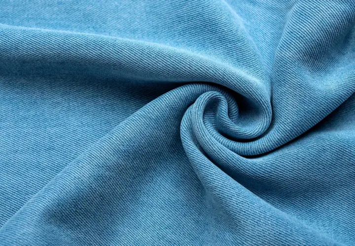Miękka, błękitna tkanina lyocellu z charakterystycznym splotem, ułożona w eleganckie fale i spiralę.
