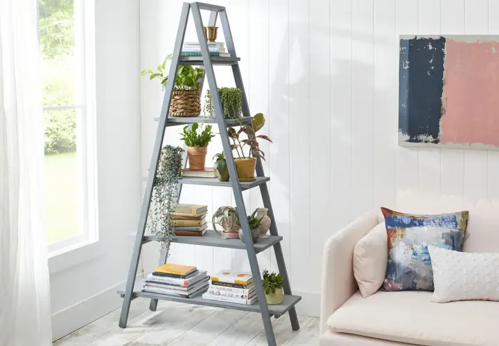 Perchero escalera gris con plantas y libros, junto a un sofá rosa.
