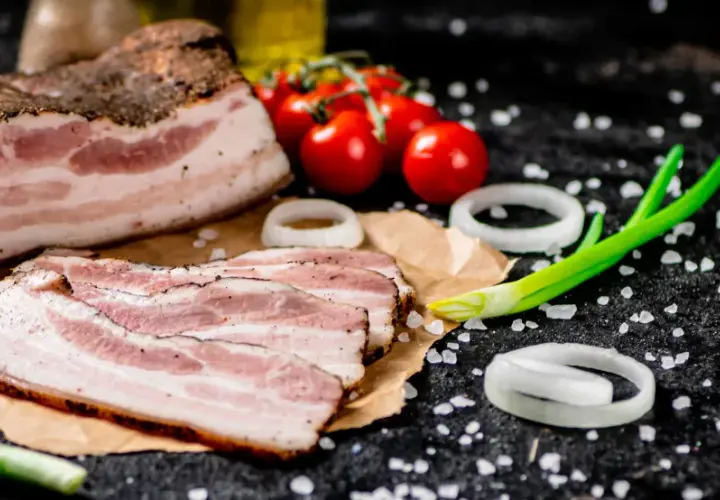 Idealny boczek do carbonary: plastry wędzonego boczku, pomidorki, cebula i szczypiorek na czarnym tle.