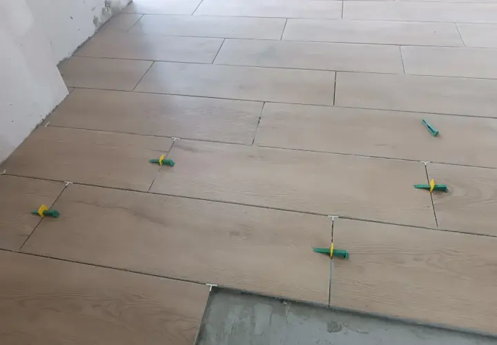 Posa di piastrelle effetto legno con distanziatori verdi. Ottenere preventivi per i prezzi piastrellista al mq è fondamentale per un lavoro ben fatto.