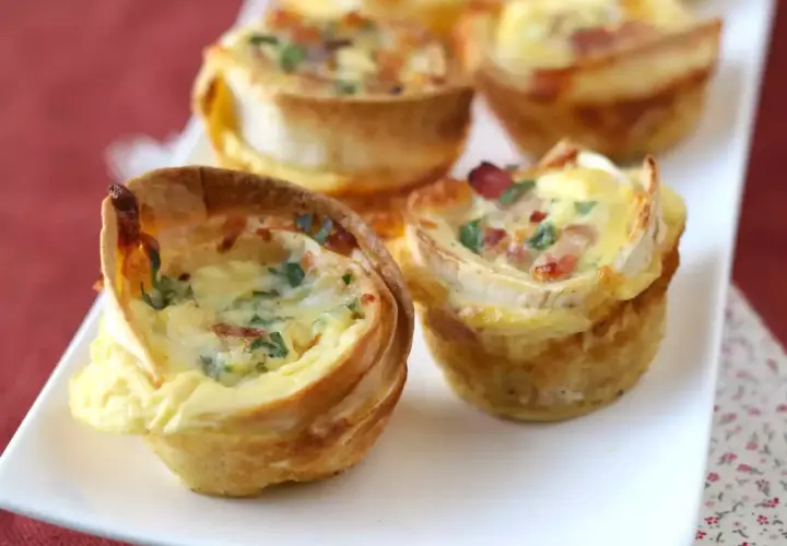 Petits quiches wraps dorés, garnis d'œufs, de lardons et de persil, servis sur une assiette blanche.