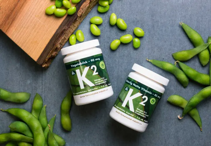 Zwei Flaschen Vitamin K2, umgeben von frischen Edamame-Bohnen. Vegane K2-Lebensmittel für gesunde Knochen.