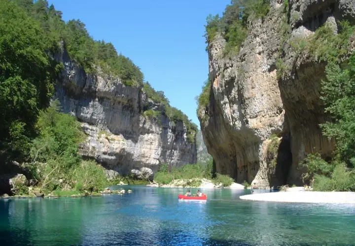 Spływ kajakiem po turkusowej rzece w wąwozie Gorges du Tarn. Majestatyczne, skalne ściany porośnięte zielenią.