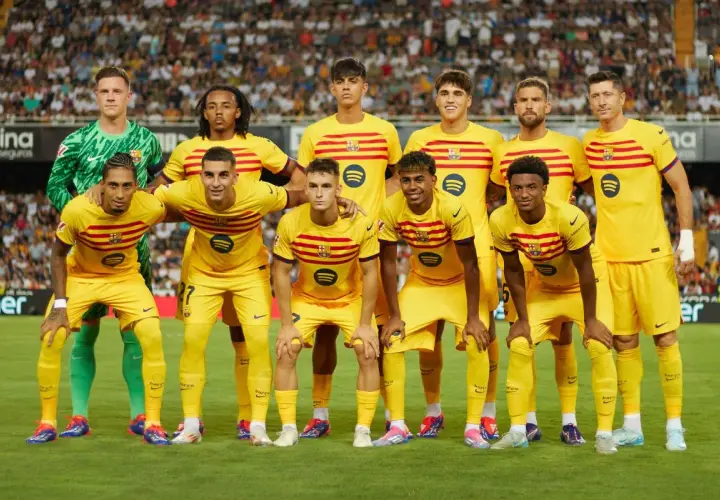 Drużyna FC Barcelona w żółtych strojach, z kapitanem na czele, pozuje do zdjęcia na tle trybun.