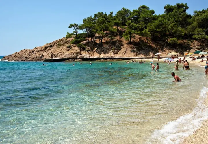 Słoneczna plaża na Thassos, z turkusową wodą i skalistym wybrzeżem. Ludzie kąpią się i odpoczywają, ciesząc się urokami wyspy. To idealne miejsce na wakacje, pełne atrakcji.