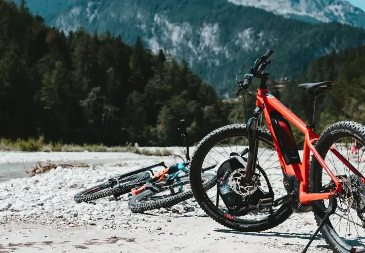 Aventura en Croacia en bicicleta, con bicicletas de montaña listas junto a un río pedregoso y un bosque frondoso.