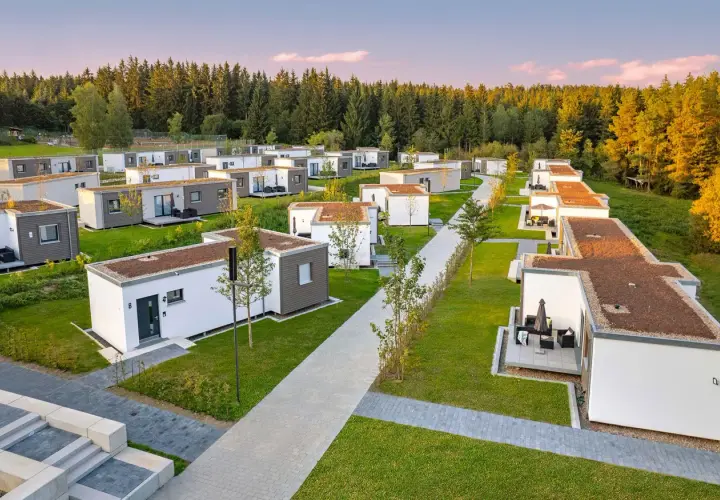 Reihe von kleinen Häusern, modern und minimalistisch, mit begrünten Dächern, eingebettet in eine grüne Landschaft am Waldrand.