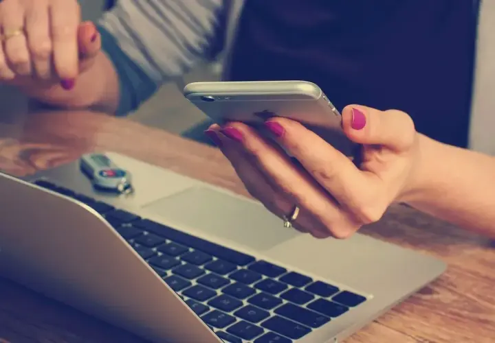 Kobieta z różowym lakierem na paznokciach trzyma telefon, obok laptopa. Szybko dzwoni na infolinię Energa Obrót, by rozwiązać sprawę.