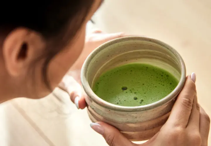 Frau hält eine Schale mit schaumigem, leuchtend grünem Matcha. Die ideale matcha temperatur für den perfekten Genuss.