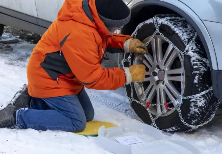 Persona con guantes ajusta la cadena del coche a la rueda cubierta de nieve.
