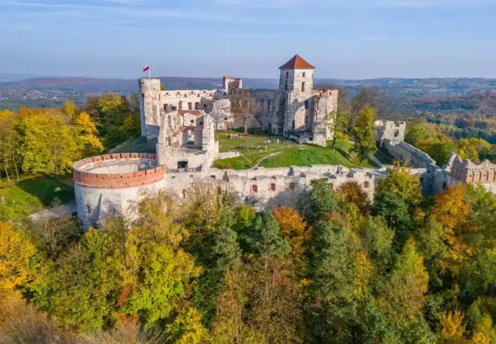 Ruiny zamków Orlich Gniazd na wzgórzu, otoczone jesiennym lasem. Polska flaga powiewa na wieży.