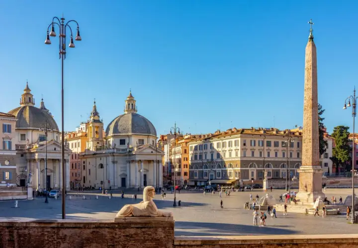 La Piazza del Popolo à Rome, avec ses églises jumelles, son obélisque et son sphinx, sous un ciel bleu éclatant.