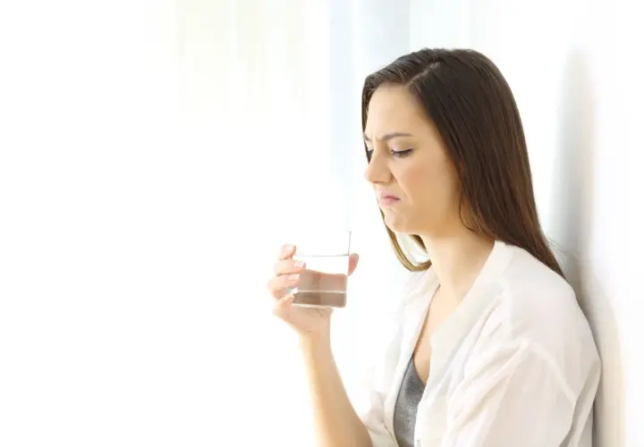 Donna con espressione disgustata tiene un bicchiere d'acqua, avvertendo un sapore metallico in bocca.
