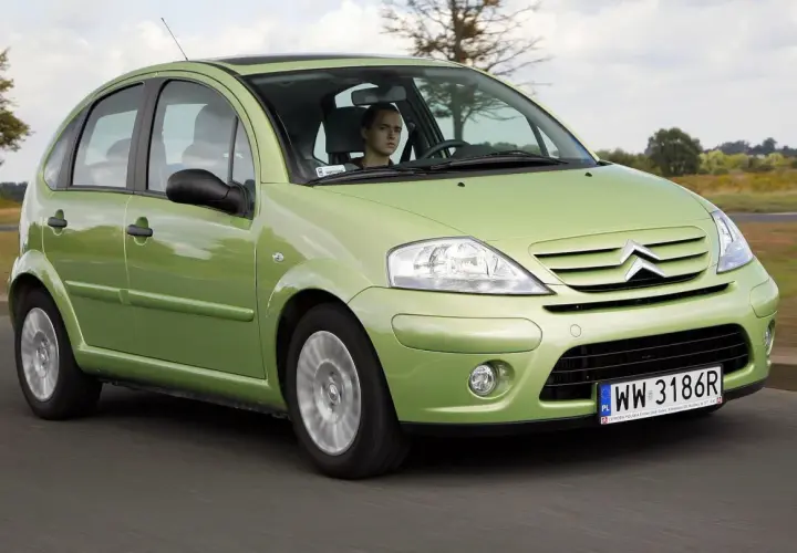 Zielony Citroen C3 2005 z młodym kierowcą za kierownicą przemierza wiejską drogę.