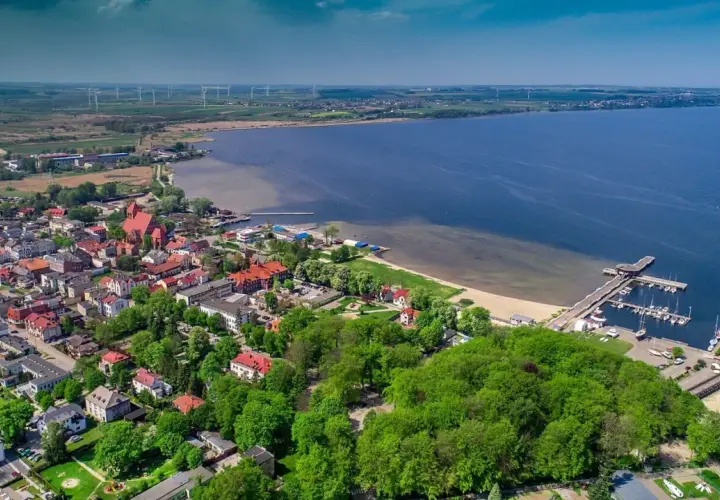 Widok z lotu ptaka na miasto nad Zatoką Pucką, z portem jachtowym, plażą i wiatrakami na horyzoncie.