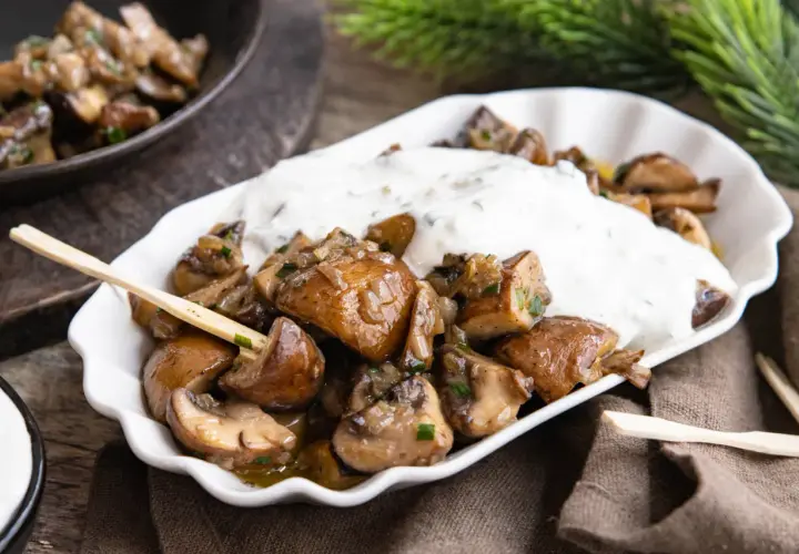 Gebratene Champignons mit Kräuterquark, wie vom Weihnachtsmarkt, auf einem weißen Teller mit Holzspießen.