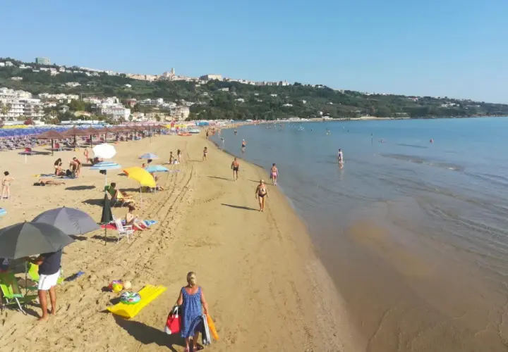 Plage animée à Vasto, Italie, avec des parasols colorés, des baigneurs et une ville en arrière-plan.