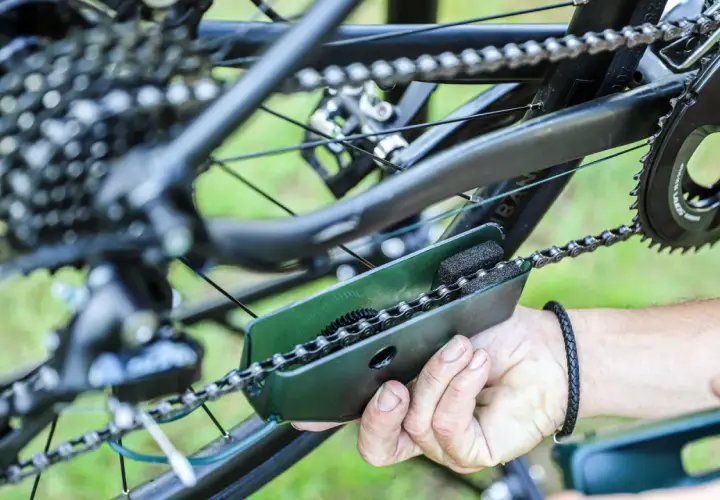 Czyszczenie łańcucha rowerowego za pomocą specjalnego narzędzia. Widać mechanizm przerzutek i zębatki.