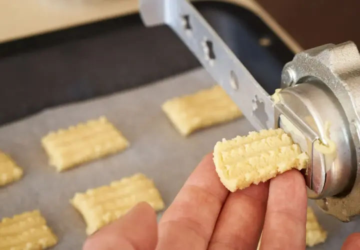 Ręka trzyma świeżo wyciśnięte ciastka z maszynki, gotowe do pieczenia.