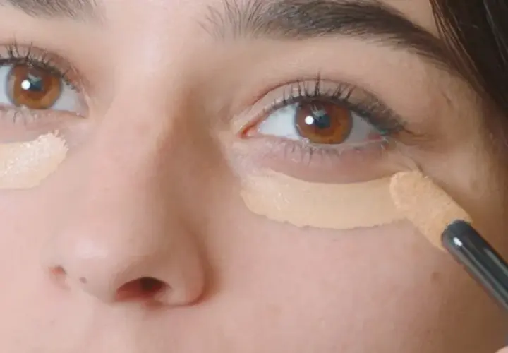 Aplicando corrector para disimular las ojeras antes o después del maquillaje.