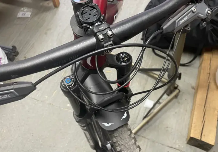 Close-up of a mountain bike's handlebars and front fork, showing the brake levers and the neat routing of the cutting hydraulic hose.