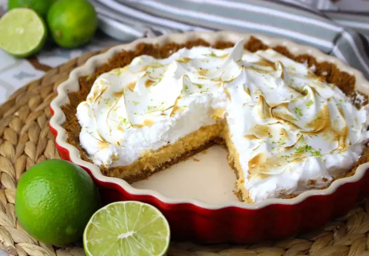 Delicioso key lime pie con merengue dorado y ralladura de lima, acompañado de limas frescas.
