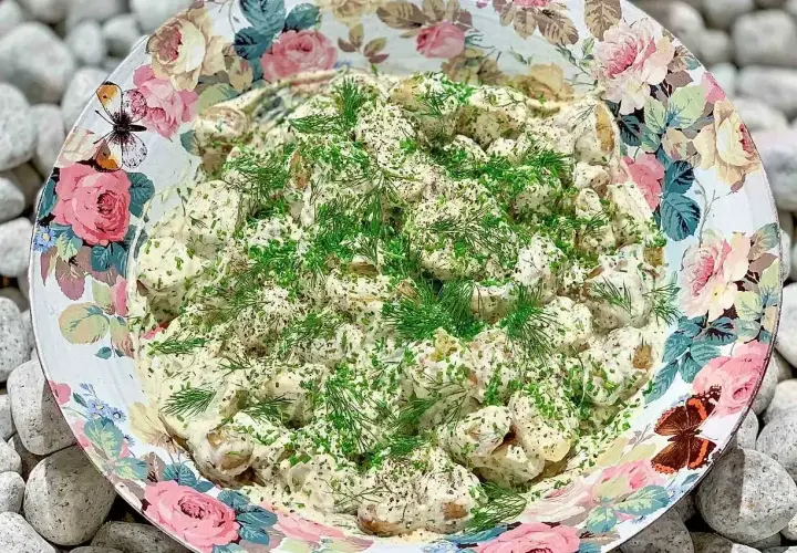 En stor skål med krämig potatissallad, toppad med dill och gräslök. Den vackra skålen har ett blommönster med fjärilar. Detta är nog den godaste potatissalladen!