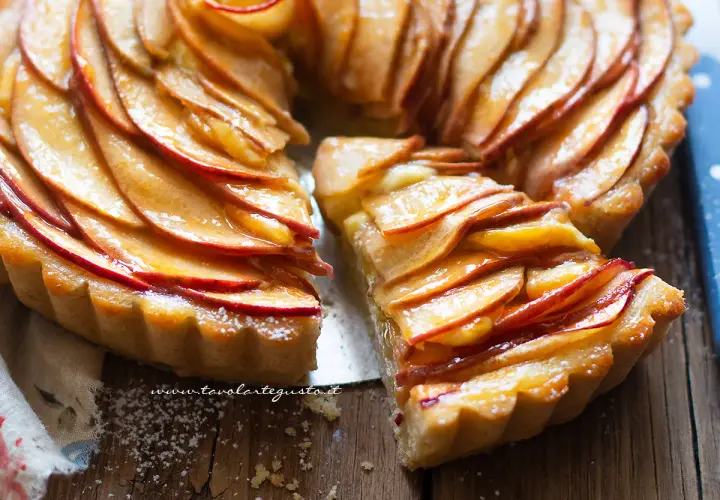 Una deliziosa crostata di mele, con le fette di mela disposte a rosa e lucide di glassa, su un tagliere di legno.
