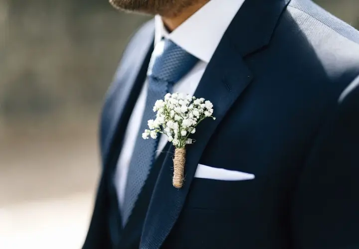 Elegancki granatowy garnitur z niebieskim krawatem, białą poszetką i bukiecikiem gipsówki.