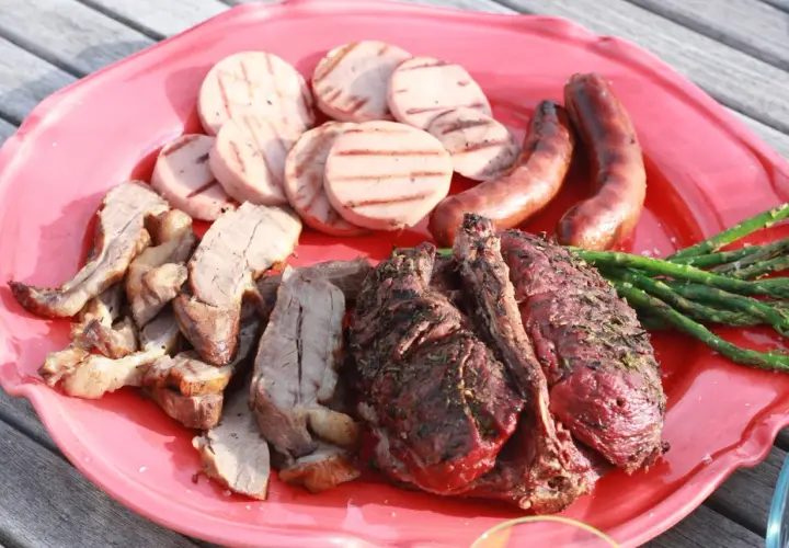 En stor röd bricka med grillad rådjur, korv, grillad korv och sparris. En härlig sommarmåltid!