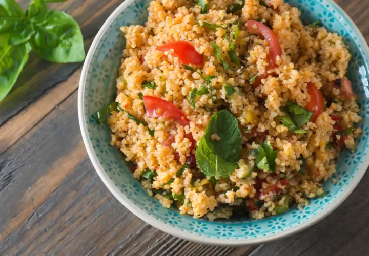 Una ciotola di insalata di cous cous con pomodorini e erbe fresche, pronta per essere gustata.