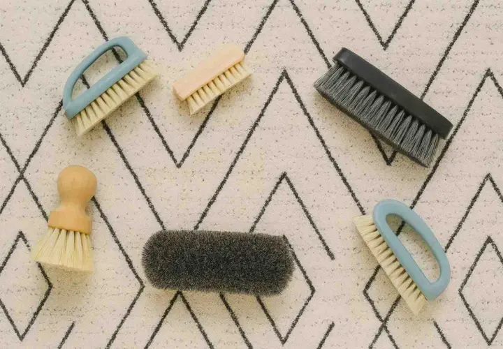 Cinco cepillos de diferentes tamaños y colores sobre una alfombra con patrón de zigzag. Herramientas perfectas para saber como limpiar alfombras a mano.