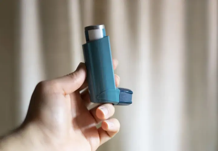 Dłoń trzyma niebieski inhalator z salbutamolem, gotowy do ulgi w astmie.