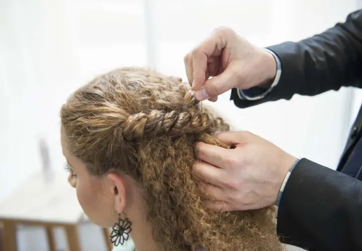 Hårstylist flätar en del av en kvinnas lockiga hår. En bra frisyr kan ge inspiration för hur man får lockigt hår.