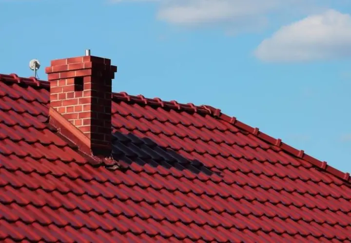 Roter Ziegeldach mit einem gemauerten Kamin. Die Anschlussstelle zwischen Kamin und Dach scheint undicht zu sein.