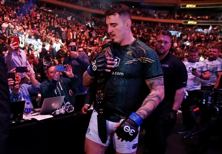 Mistrz UFC z pasem na ramieniu, otoczony tłumem fanów robiących zdjęcia.