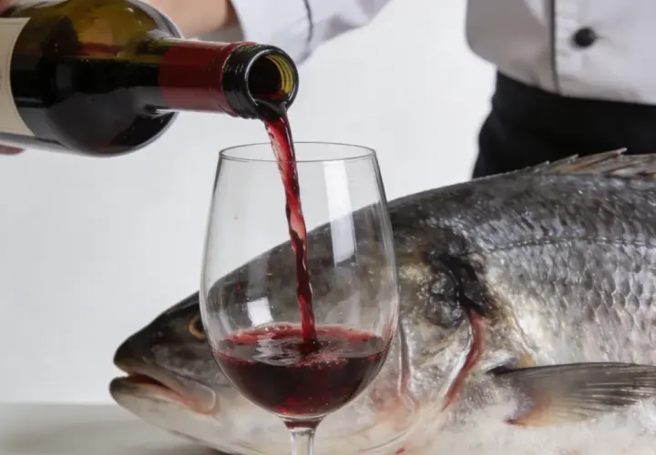 Un chef verse du vin rouge dans un verre, à côté d'un poisson entier. Une question se pose : quel vin rouge avec du poisson ?