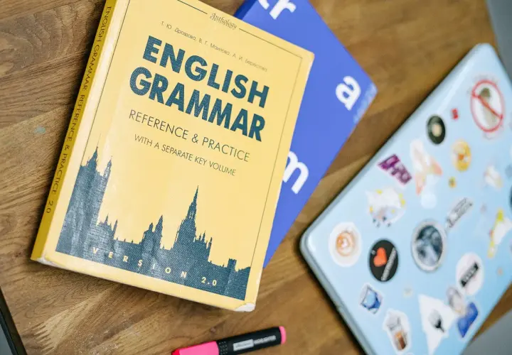 Książka "English Grammar: Reference & Practice" i niebieski notatnik leżą na drewnianym blacie. Idealne do nauki zadań gramatycznych angielskiego.