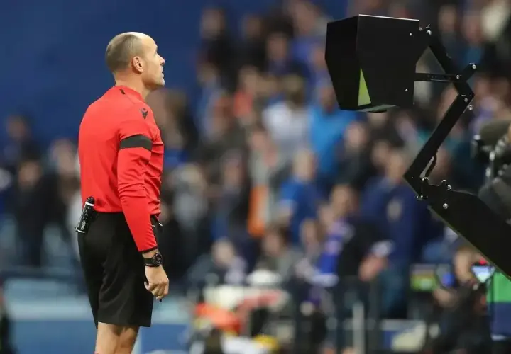 Sędzia w czerwonej koszulce czeka na decyzję VAR, która może skutkować żółtą kartką.